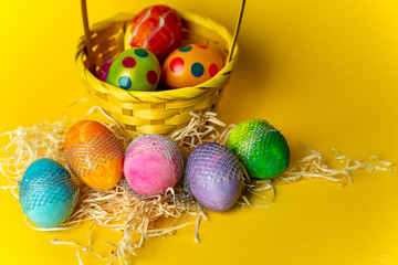 colorful, hand-painted, pastel Easter eggs in a basket on a bright, yellow, spring background