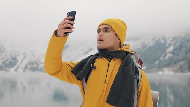 Hiker man using smartphone taking a photo of winter nature. The tourist admires nature and makes photos.Young man standing against the background of beautiful mountains