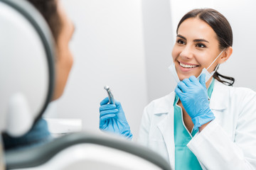 smiling female stomatologist holding drill near patient