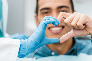 selective focus of dentist and african american patient hands making heart shape