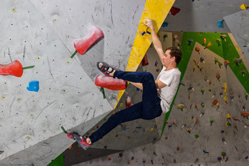 Rock climber man hanging on a bouldering climbing wall, inside on colored hooks