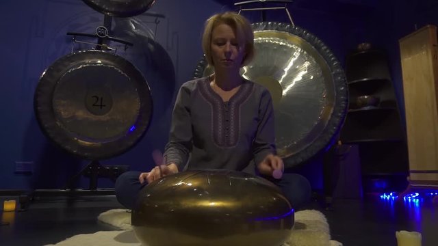 Woman is playing meditative instrument tank drum in a dark meditation room.