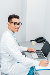 cheerful african american doctor making notes and using laptop