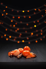 Christmas composition. Mandarins and cinnamon on black background of blurred defocused multicolor lights. Christmas, winter, new year concept.