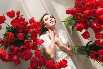 A beautiful young girl in a peignoir is lying on the floor between large bouquets of tulips. March 8 concept.