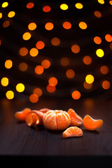 Christmas composition. Mandarins, tangerine slices, tangerine peel on black background of blurred defocused multicolor lights. Christmas, winter, new year concept.