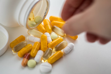 Frau nimmt Pillendose mit gelben und weißen Pillen Kapseln und Tabletten auf weißen Hintergrund