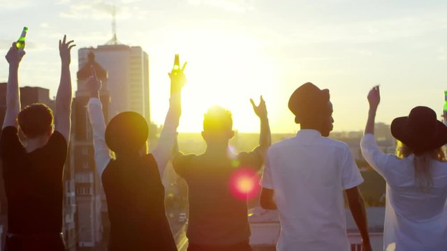 Rear view of group of young hipster friends holding beer bottles while standing on urban rooftop