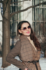 Street style Fashion portrait pretty young woman in trendy casual clothes, smiling. Pullover, brown overcoat and scarf. Sunny winter day, city lifestyle. Classic look, sun glasses