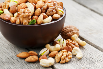 Wooden bowl with mixed nuts on a wooden gray background. Walnut, pistachios, almonds, hazelnuts and cashews, walnut.