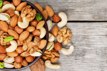Wooden bowl with mixed nuts on a wooden gray background. Walnut, pistachios, almonds, hazelnuts and...