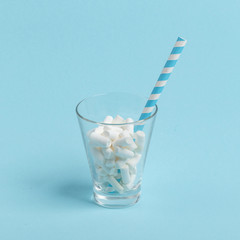 Glass cup with paper tube and marshmallows on a blue background. Minimalistic concept.