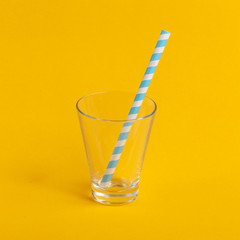 Glass cup with paper tube on a yellow background. Minimalistic concept.