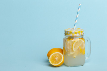 A jar of homemade lemonade and lemons on a blue background.
