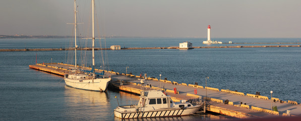 Fototapeta na wymiar Yachts at the pier on the background of the lighthouse. Panorama of the marina at sunset