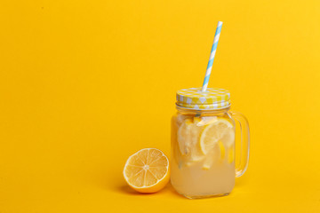 A jar of homemade lemonade and lemons on a yellow background.