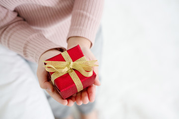 Close up of a hand holding a red gift box tied with a gold ribbon. It is a joy to celebrate the holidays, such as Valentine's Day, Christmas and Happy New Year. Concept Universal Children’s Day