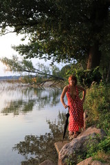 Beautiful sexy seminude woman in red dress with black umbrella near the lake.