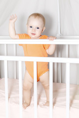 Cute baby on a tummy in a white cot looking across the room through the wooden frame, itching gums, sucking the wooden board of the cot, teething proccess. Family, baby development concept photo