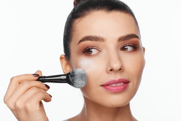 Portrait of a beautiful young woman holding a brush in her hand and applying powder to her face with a brush