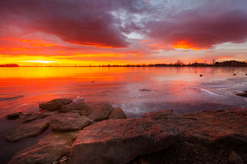 Fiery Sunrise over a Frozen Winter Lake with Rocks in the Foreground