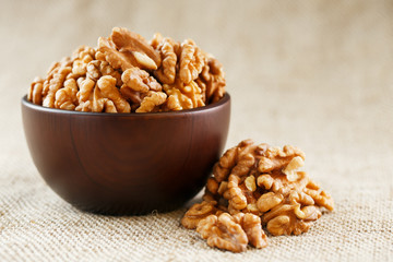Peeled walnuts in a wooden, dark brown cup on a burlap cloth.