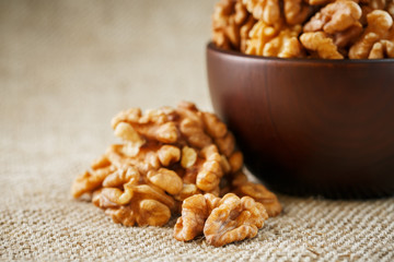Peeled walnuts in a wooden, dark brown cup on a burlap cloth.