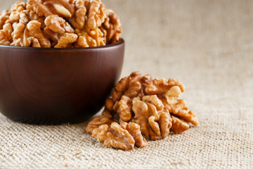 Peeled walnuts in a wooden, dark brown cup on a burlap cloth.