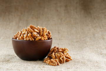 Peeled walnuts in a wooden, dark brown cup on a burlap cloth.