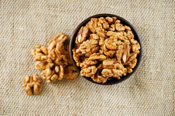 Peeled walnuts in a wooden, dark brown cup on a burlap cloth.