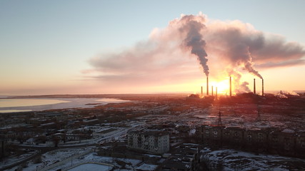 Epic sunset on the background of a Smoking factory. The red sun with bright rays goes beyond the...