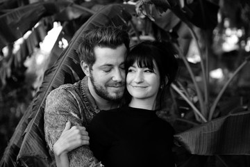 Black and White Portrait of Two Cute Modern Caucasian Beautiful Young Adult Guy Boyfriend Lady Girlfriend Couple Hugging and Kissing in Love in Nature with Green Plants Trees in the Outdoor Park