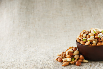 Mix of different nuts in a wooden cup against the background of fabric from burlap. Nuts as structure and background, macro. Top view.