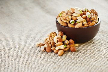 Mix of different nuts in a wooden cup against the background of fabric from burlap. Nuts as structure and background, macro. Top view.