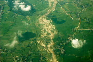 green fields and forests near the riverbed with sandy banks and the village against the white clouds. aerial photography