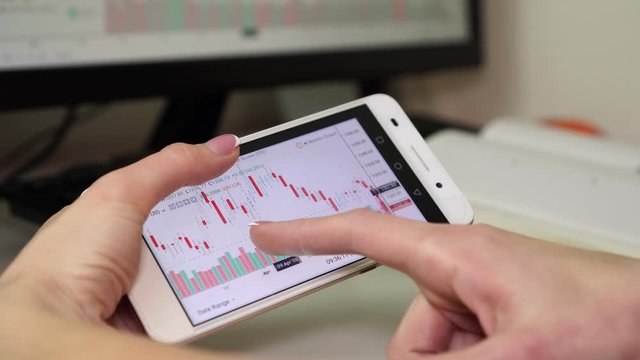 The woman analyzes the financial chart of the stock market using a smartphone.