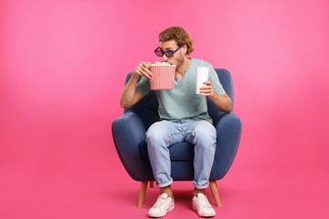 Man with 3D glasses, popcorn and beverage sitting in armchair during cinema show on color background © New Africa