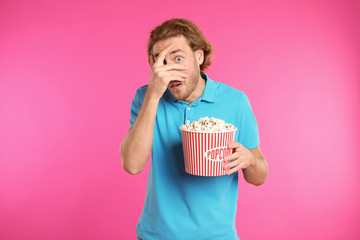 Fototapeta premium Emotional man with popcorn during cinema show on color background
