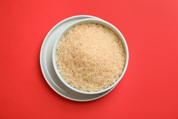 Bowl with uncooked rice on color background, top view