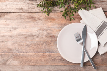 Beautiful table setting with cutlery, napkin and plate on wooden background, top view. Space for...