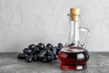Glass jug with wine vinegar and fresh grapes on gray table