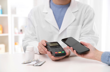 Woman using terminal for contactless payment with smartphone in pharmacy, closeup