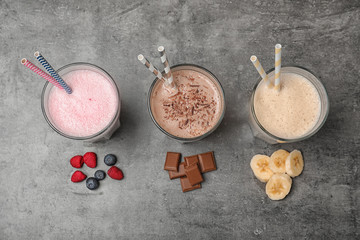 Glasses with different protein shakes and ingredients on grey background, top view