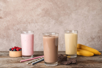 Glasses with different protein shakes and ingredients on table against color background