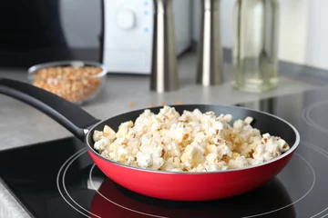 Poster Frying pan with tasty popcorn on stove in kitchen © New Africa