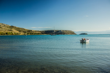 Naklejka premium cozy sea bay calm water surface with small empty fishing boat in morning fresh sun rise time, south Europe scenic natural landscape