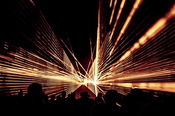 Golden laser show nightlife club stage with party people crowd. Luxury entertainment with audience silhouettes in nightclub event, festival or New Year's Eve. Beams and rays shining colorful lights