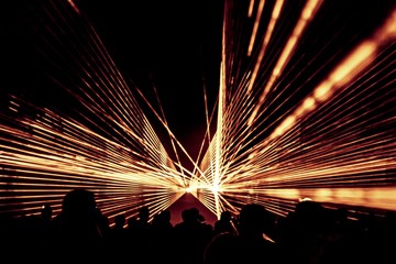 Golden laser show nightlife club stage with party people crowd. Luxury entertainment with audience silhouettes in nightclub event, festival or New Year's Eve. Beams and rays shining colorful lights © azur13