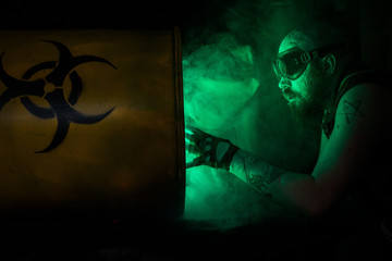Photo of a bearded male with smoking bio-hazard barrel, strong dystopian/post apocalyptic vibes.