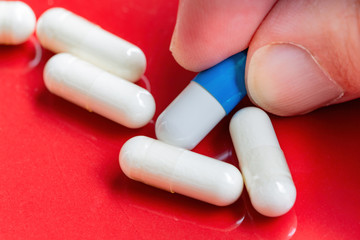 fingers catching a blue and white pill on red background